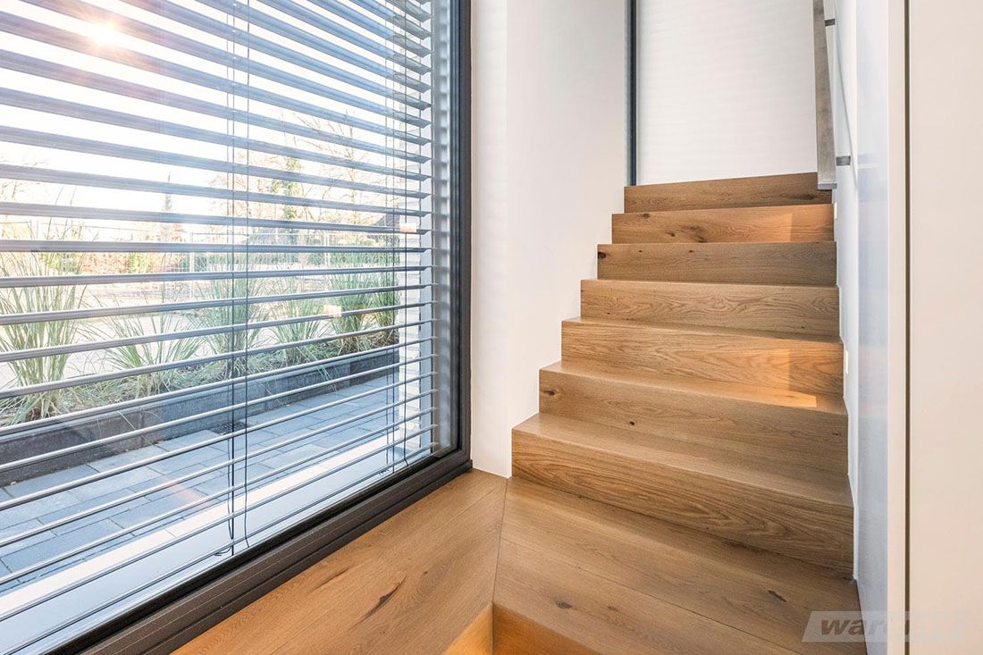 Holztreppe neben großem Fenster mit geöffnetem Raffstore, Blick auf Garten mit Pflanzen